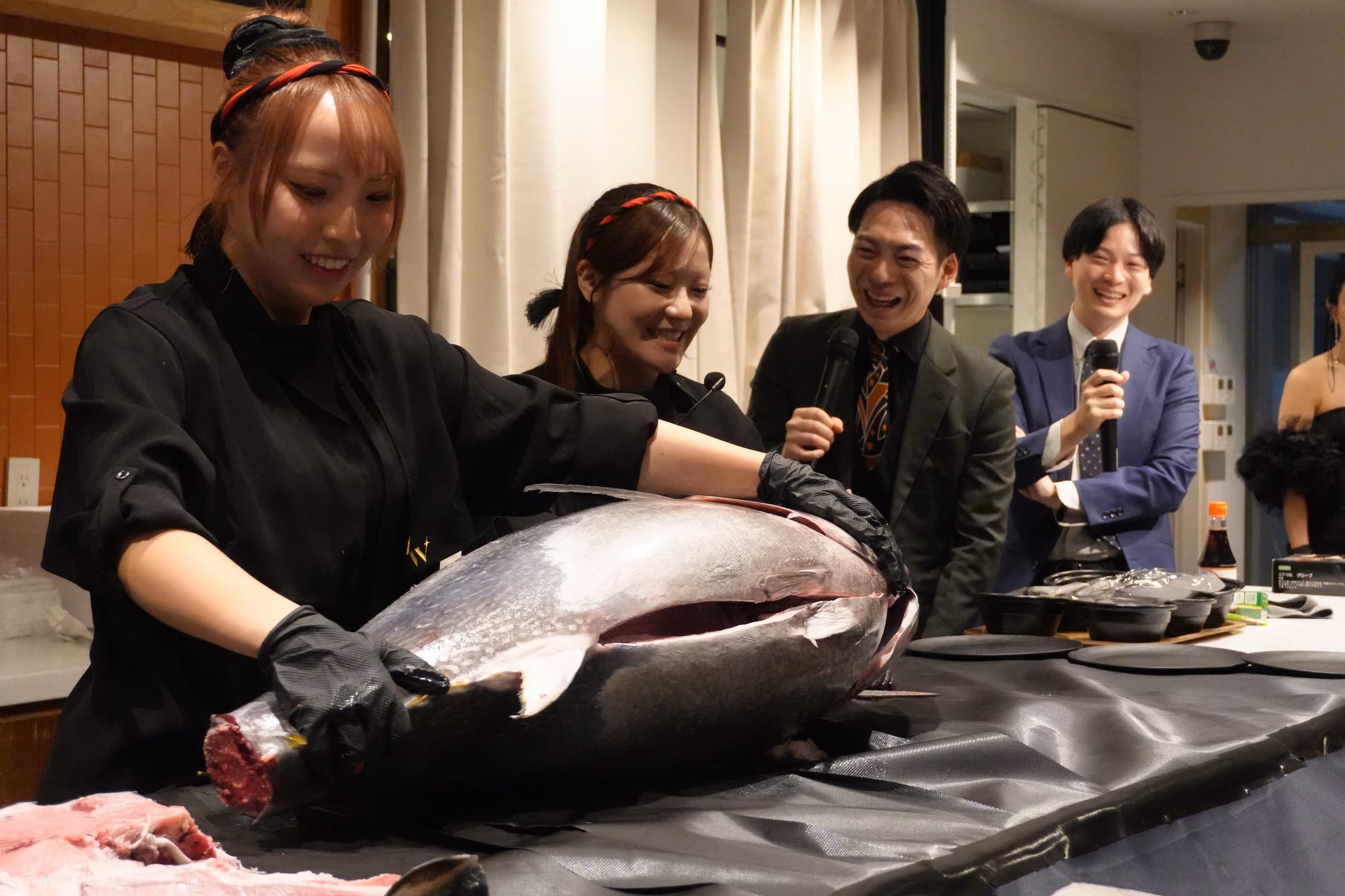 女性解体師がマグロに包丁を入れ、観客が取り囲む解体ショーの場面