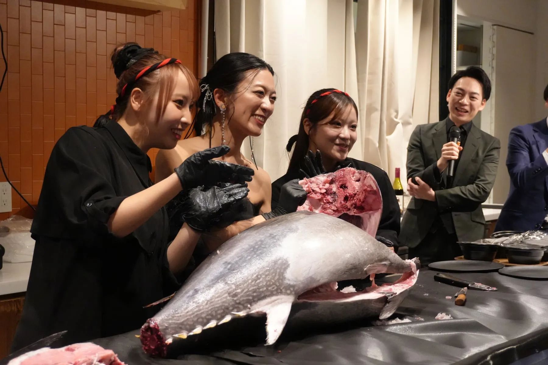 参加者がマグロを囲み、スタッフとMCが進行する場面