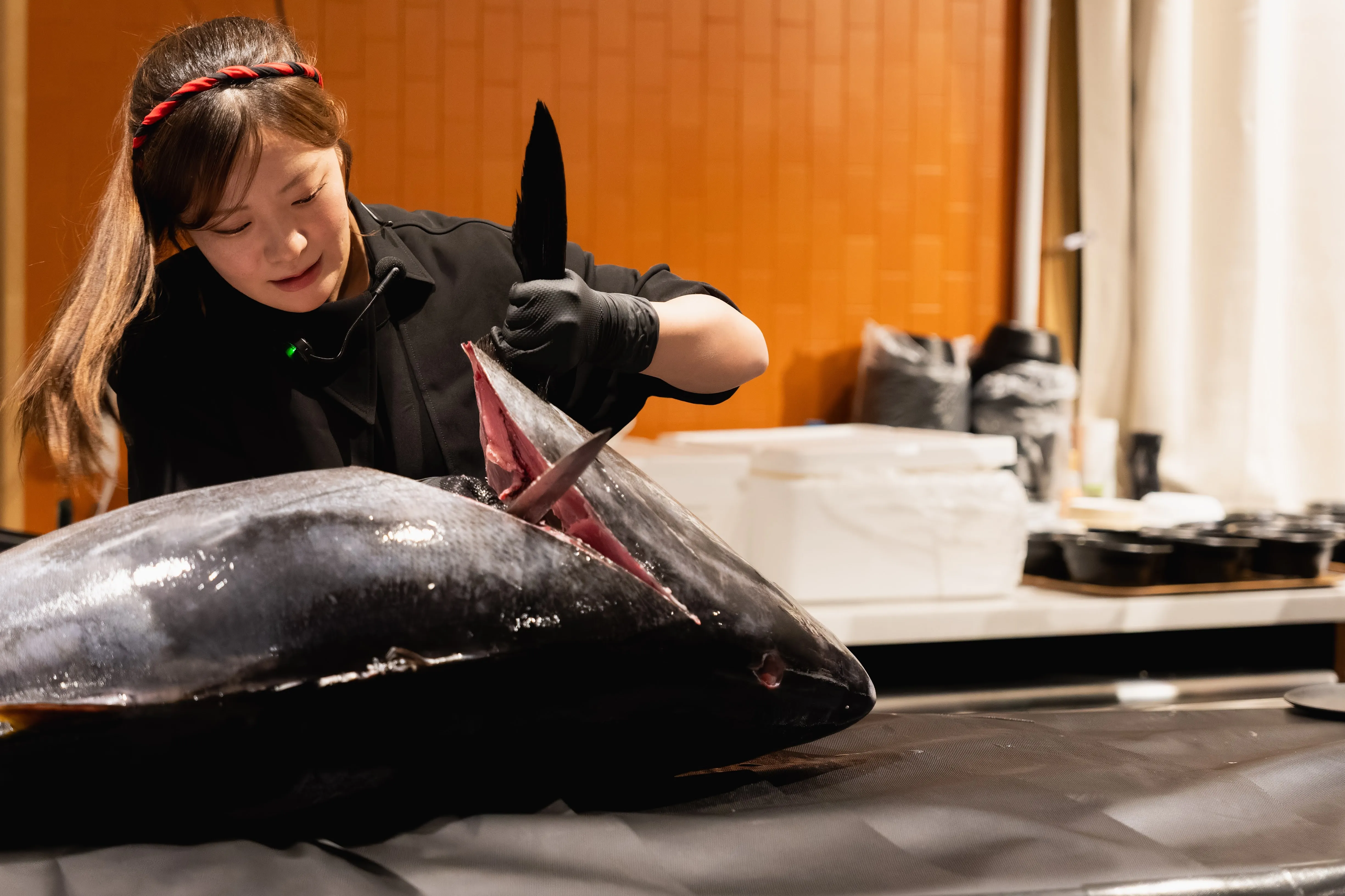 女性解体師がマグロのカマ部分に包丁を入れる場面
