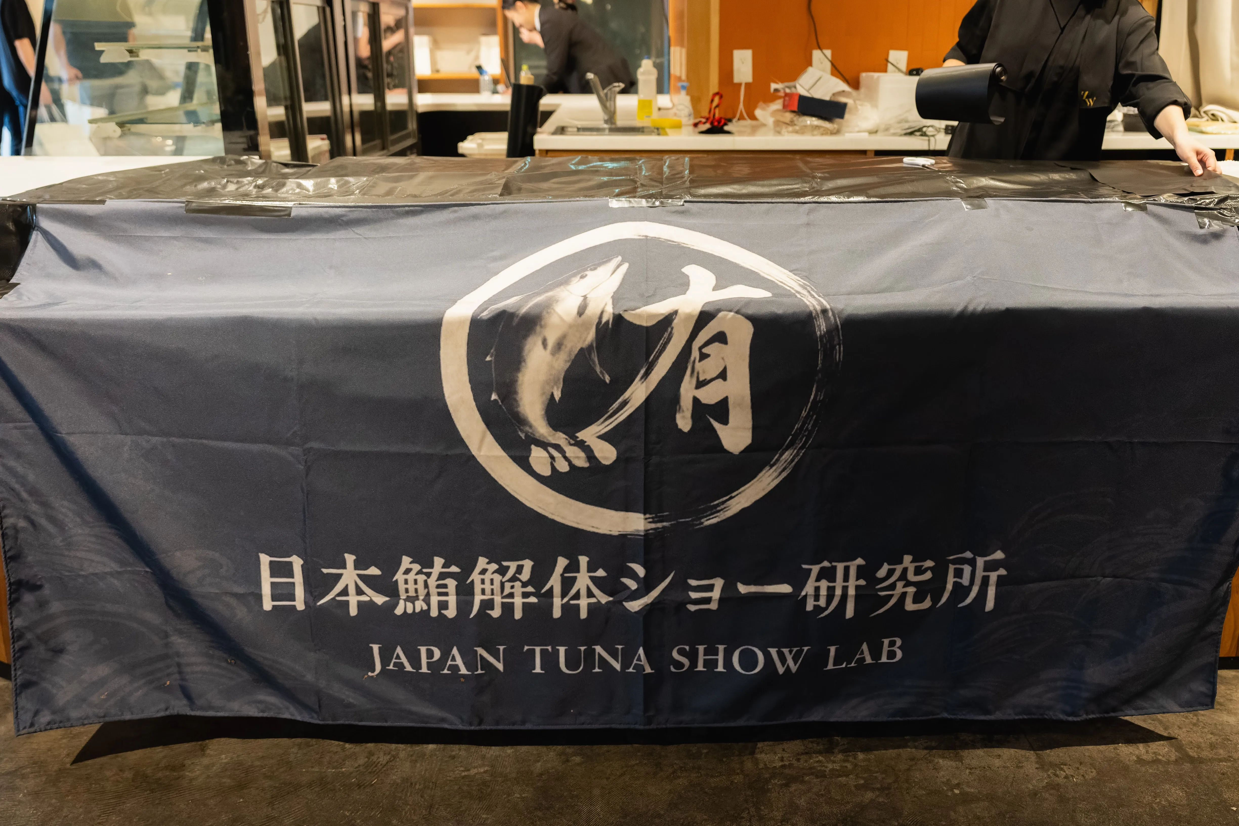 解体台に養生シートを設置し、会場を保護する準備の場面