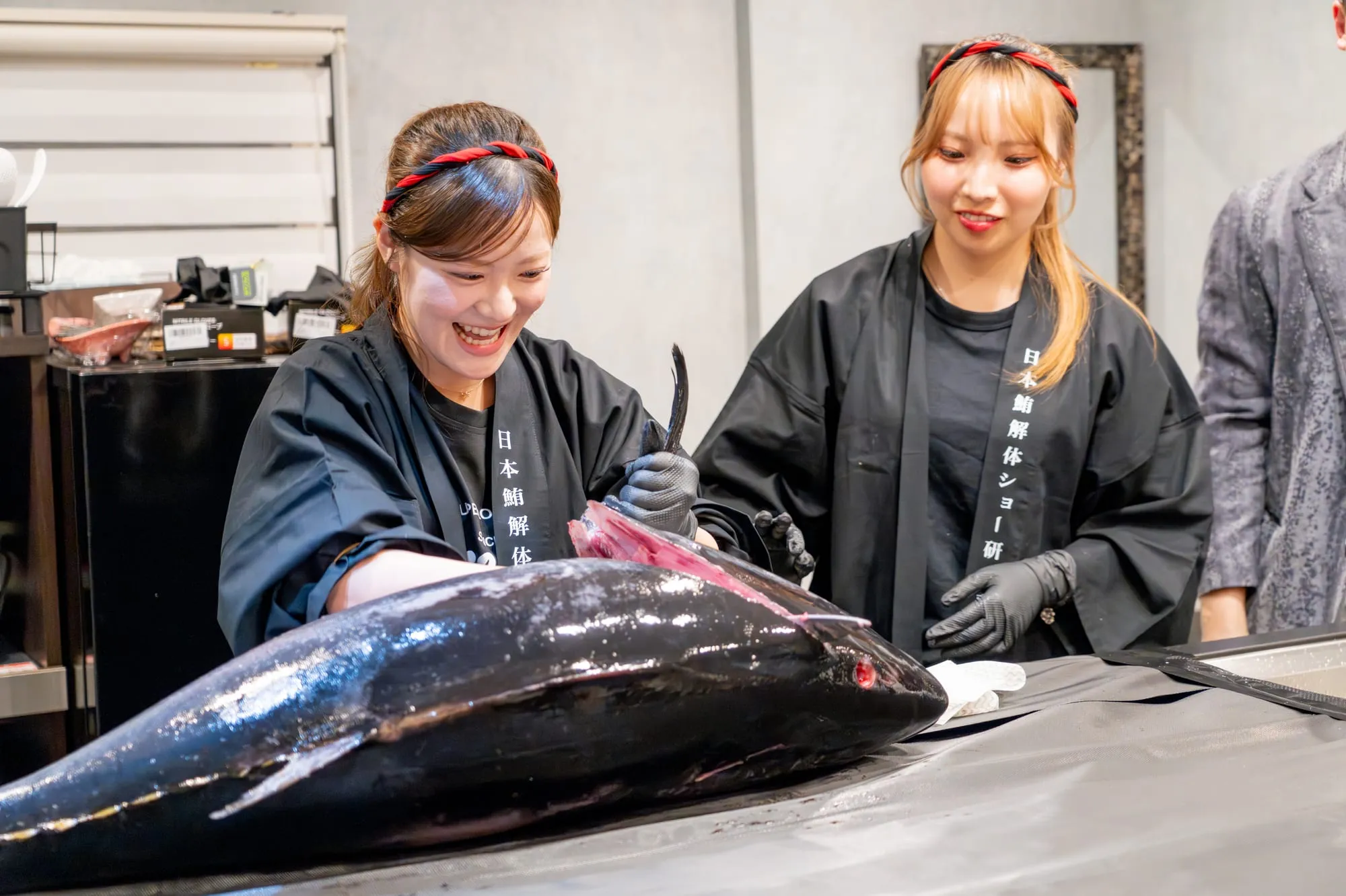 解体前の生本マグロを前に立つ女性解体師2名