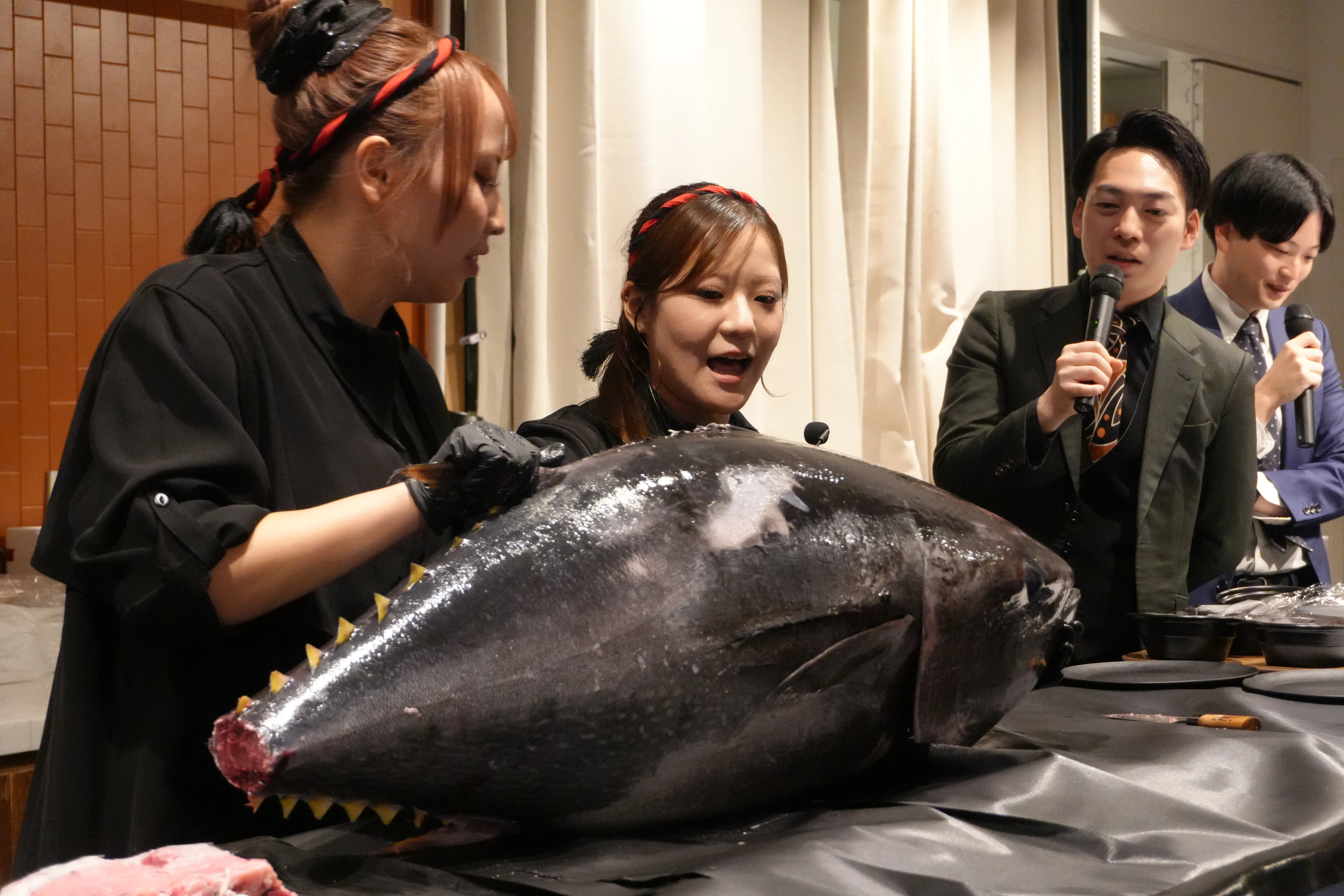 女性解体師2名がマグロを掲げ、MC2名が進行する場面
